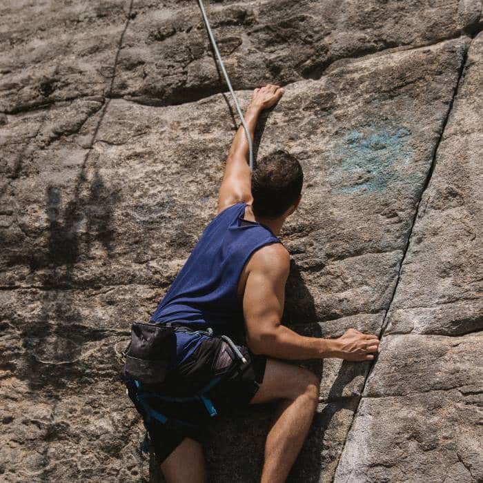 A climber ascending a rock face with a rope and climbing chalk bag.