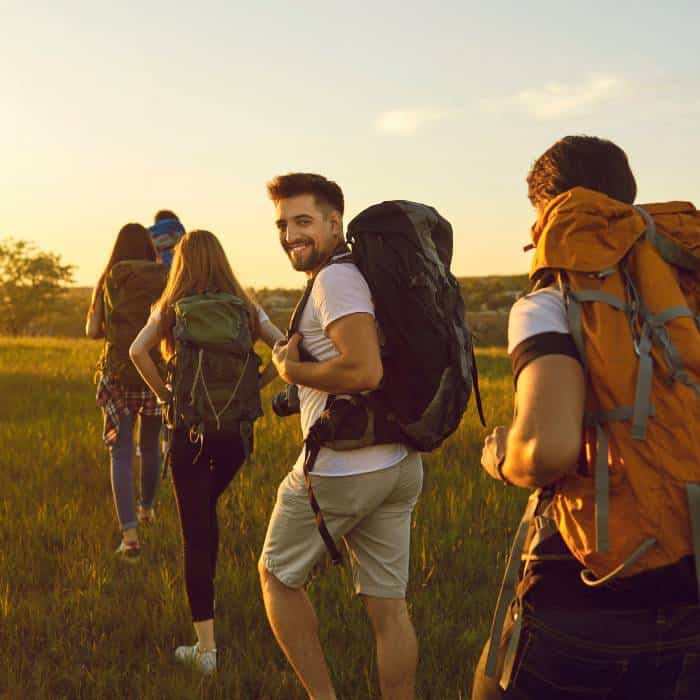 A group of happy hikers with backpacks enjoying a sunny trek through a grassy field.