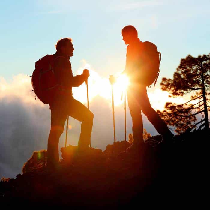Silhouettes of two hikers with poles against a sunset sky.
