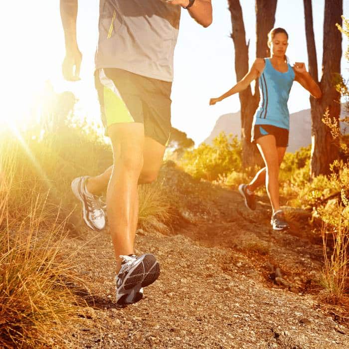 Two runners jogging on a sunlit mountain trail